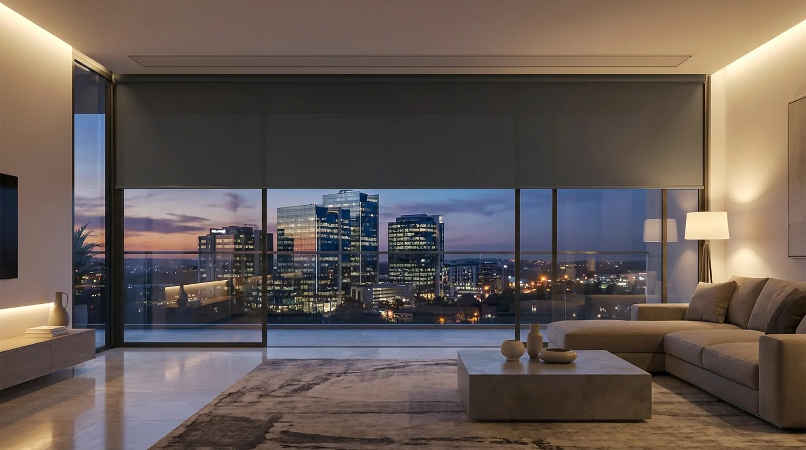 A motorised blockout roller blind as one smooth flat sheet from a recessed ceiling cassette, lowered a third of the way over floor-to-ceiling glass in a Sandton apartment looking south toward lit office towers at dusk